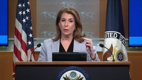 Tammy Bruce speaking at a podium with US and UN flags behind her.