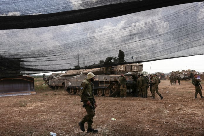 Israeli soldiers at a roadside checkpoint near the Gaza perimeter with a directional sign to Gaza visible in the background