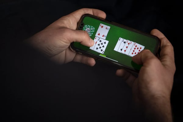 Smartphone screens showing online casino slots legalized US states revenue addiction 2025