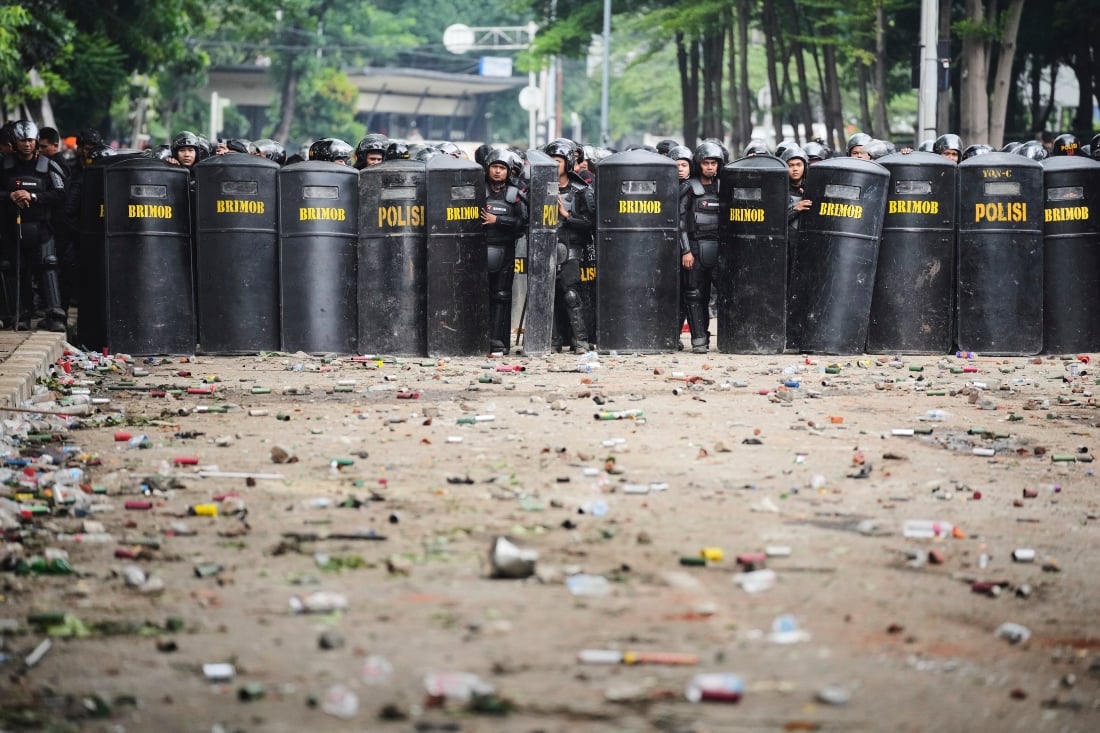 Police officers take position amid debris after protests in Jakarta