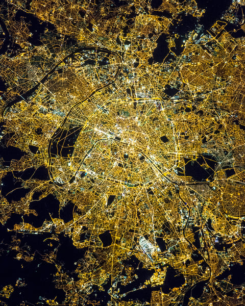 NASA astronaut photograph of Paris at night showing the Seine River as a thin black line with the bright Avenue des Champs Elysees and the radial street pattern around the Arc de Triomphe