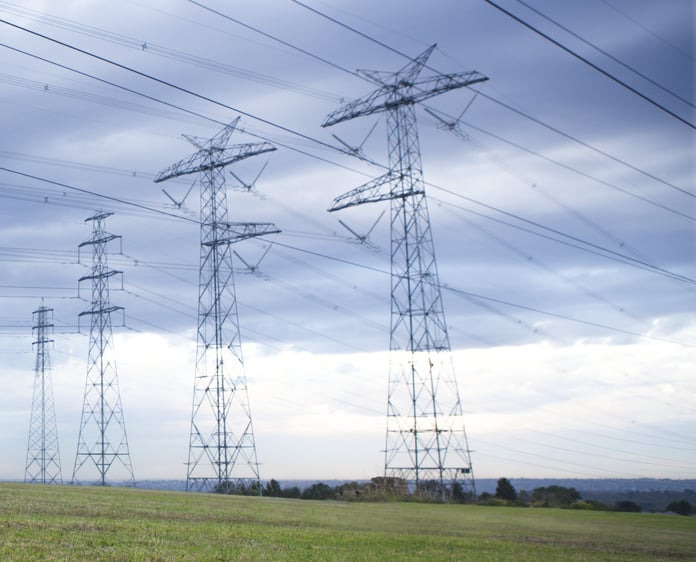 High-voltage power transmission lines against a blue sky representing the challenge of managing complex renewable energy grids