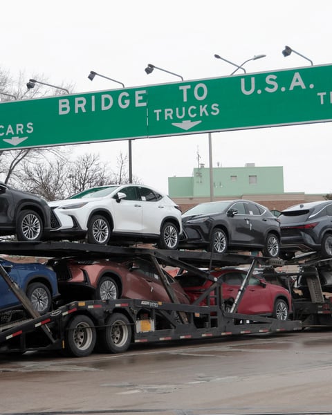 A truck transporting cars beneath signage indicating US trade routes