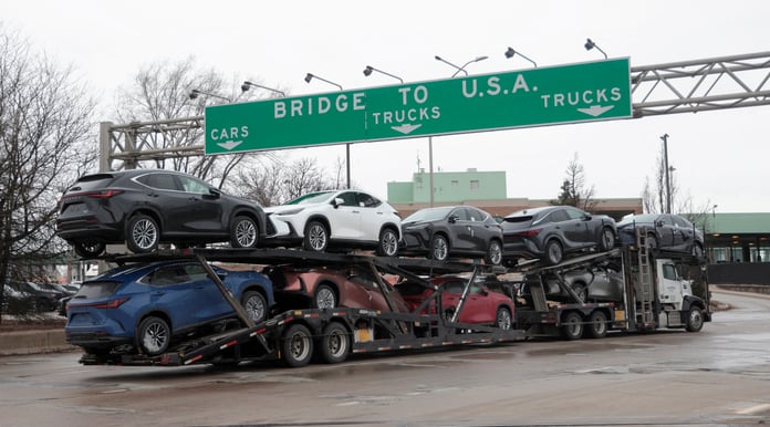 A truck transporting cars beneath signage indicating US trade routes