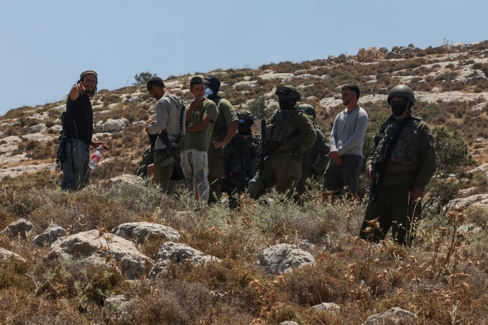 Israeli forces and armed settlers guard a bulldozer operating on Palestinian land near Dura, west of Hebron, in the occupied West Bank
