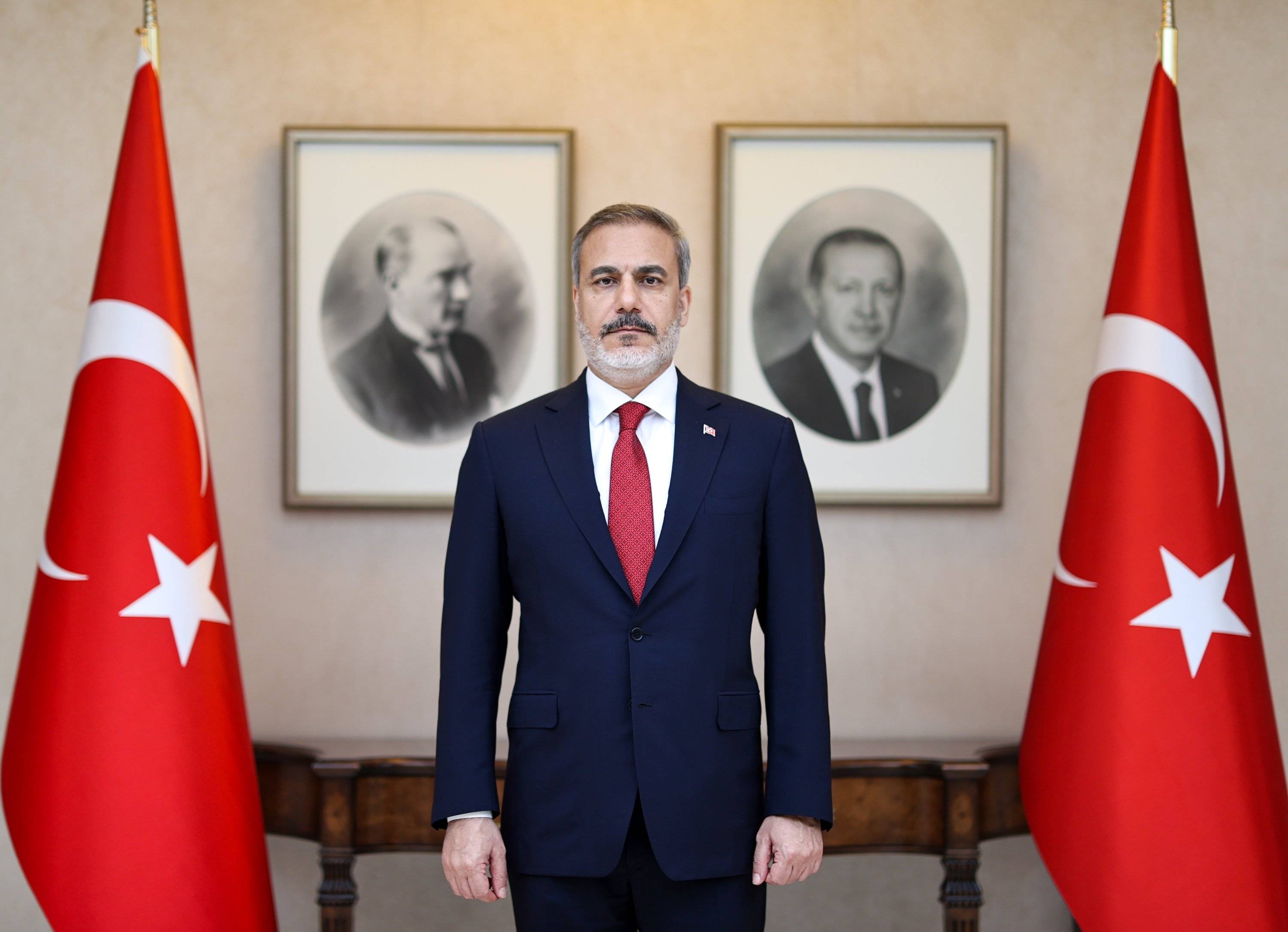 Foreign Minister Hakan Fidan is posing in front of portraits