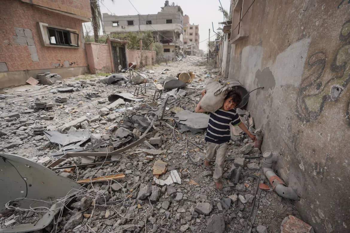 Nuseirat refugee camp street filled with debris after strikes, a child walks past ruined homes in central Gaza.