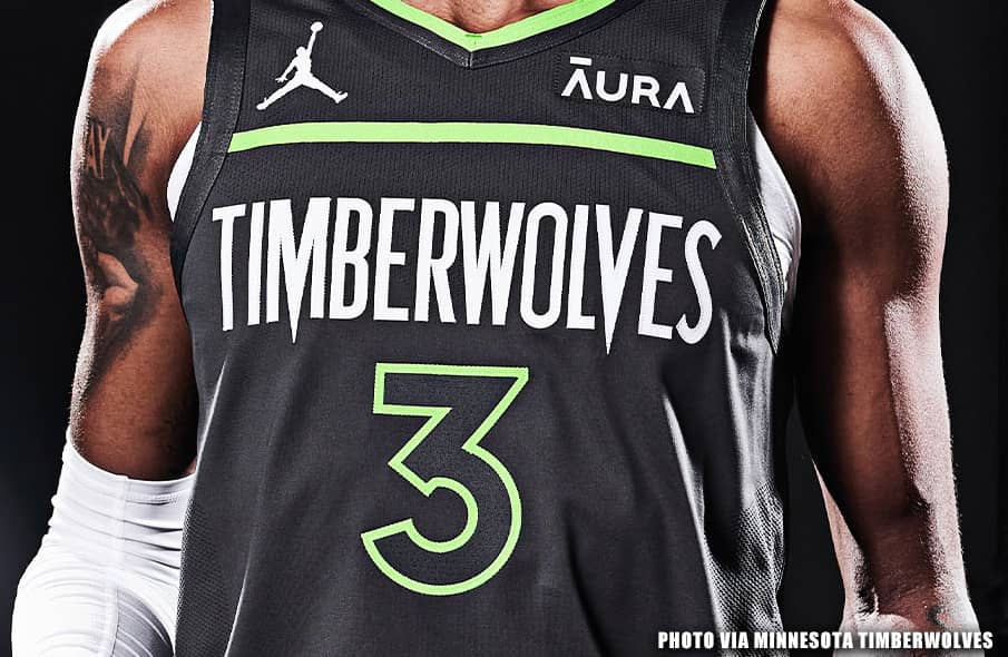 Close-up of the Minnesota Timberwolves Black Trees jersey showing the green pine-tree trim and jagged wordmark.