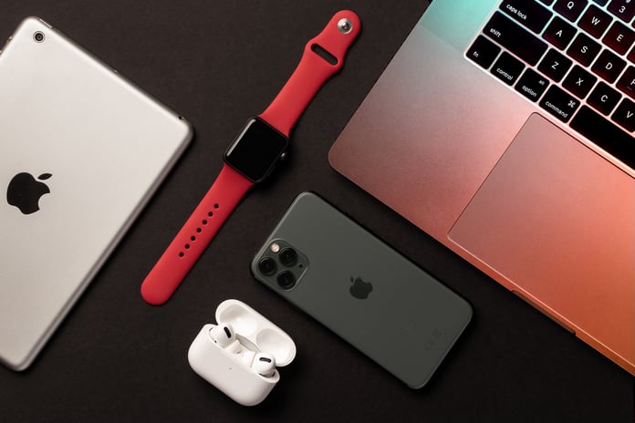 A flat lay of Apple products including iPhone MacBook and Apple Watch on a dark background