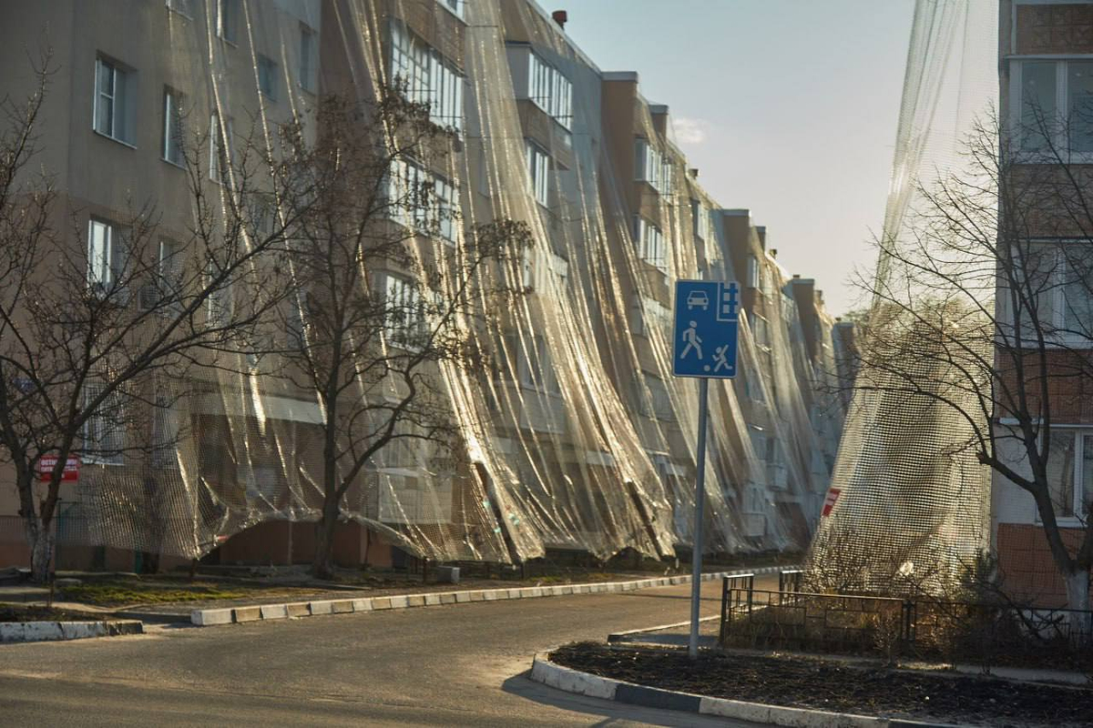 Courtyard with anti-drone netting and taped apartment windows in a frontline Ukrainian town.