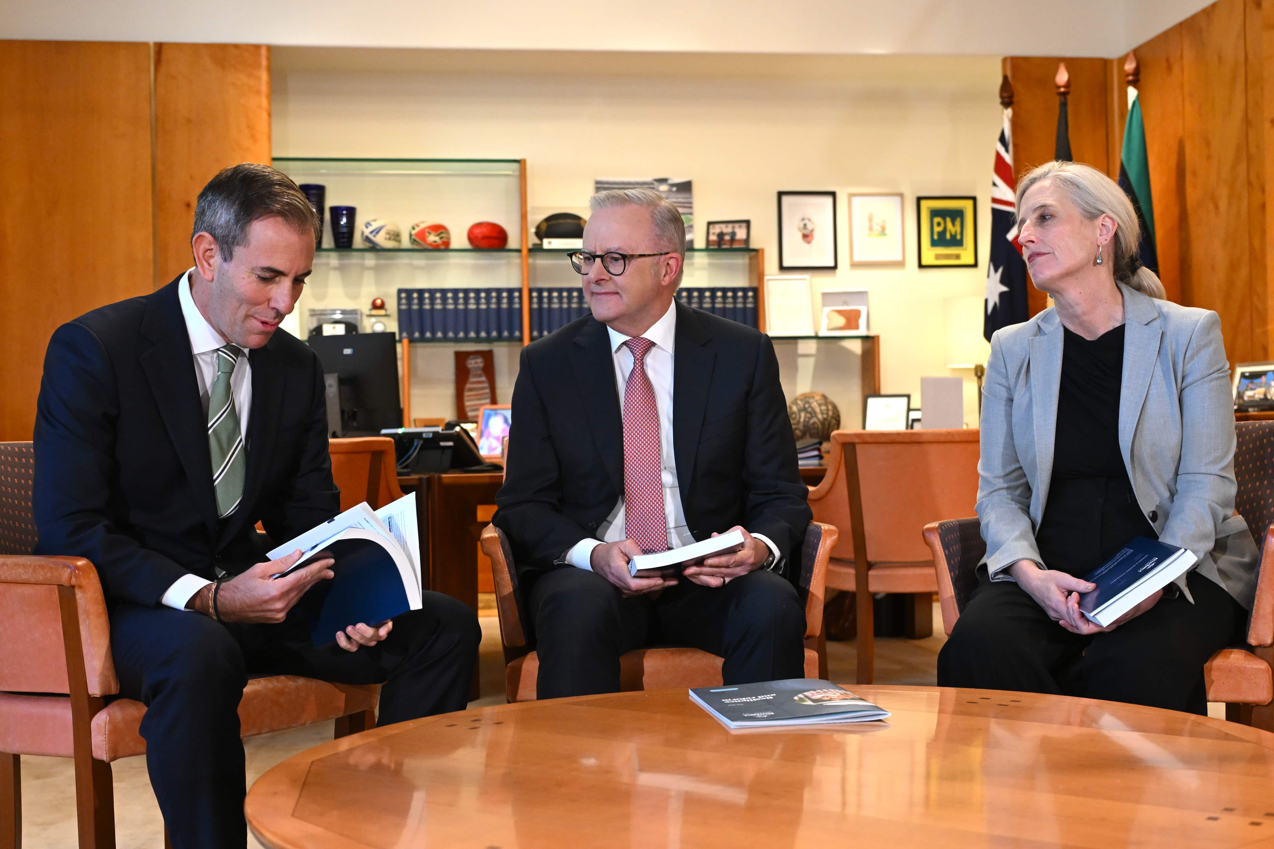 Jim Chalmers, Anthony Albanese and Katy Gallagher hold 2026 federal budget documents detailing negative gearing and capital gains tax changes
