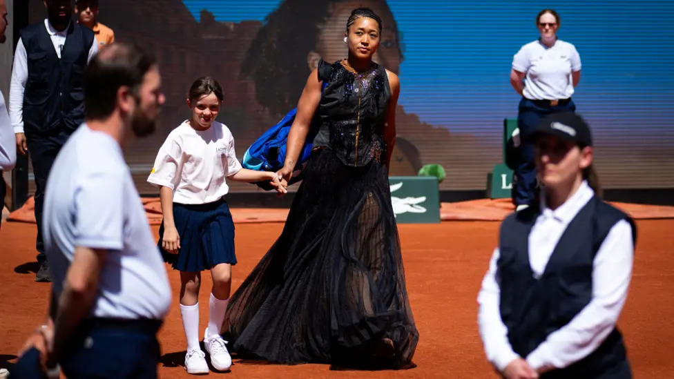Osaka Gold Match Outfit Action Shot Naomi Osaka playing tennis in gold Nike dress at Roland Garros 2026