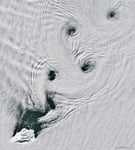 Satellite image showing von Kármán vortex streets forming spinning cloud patterns over Peter I Island in Antarctica.