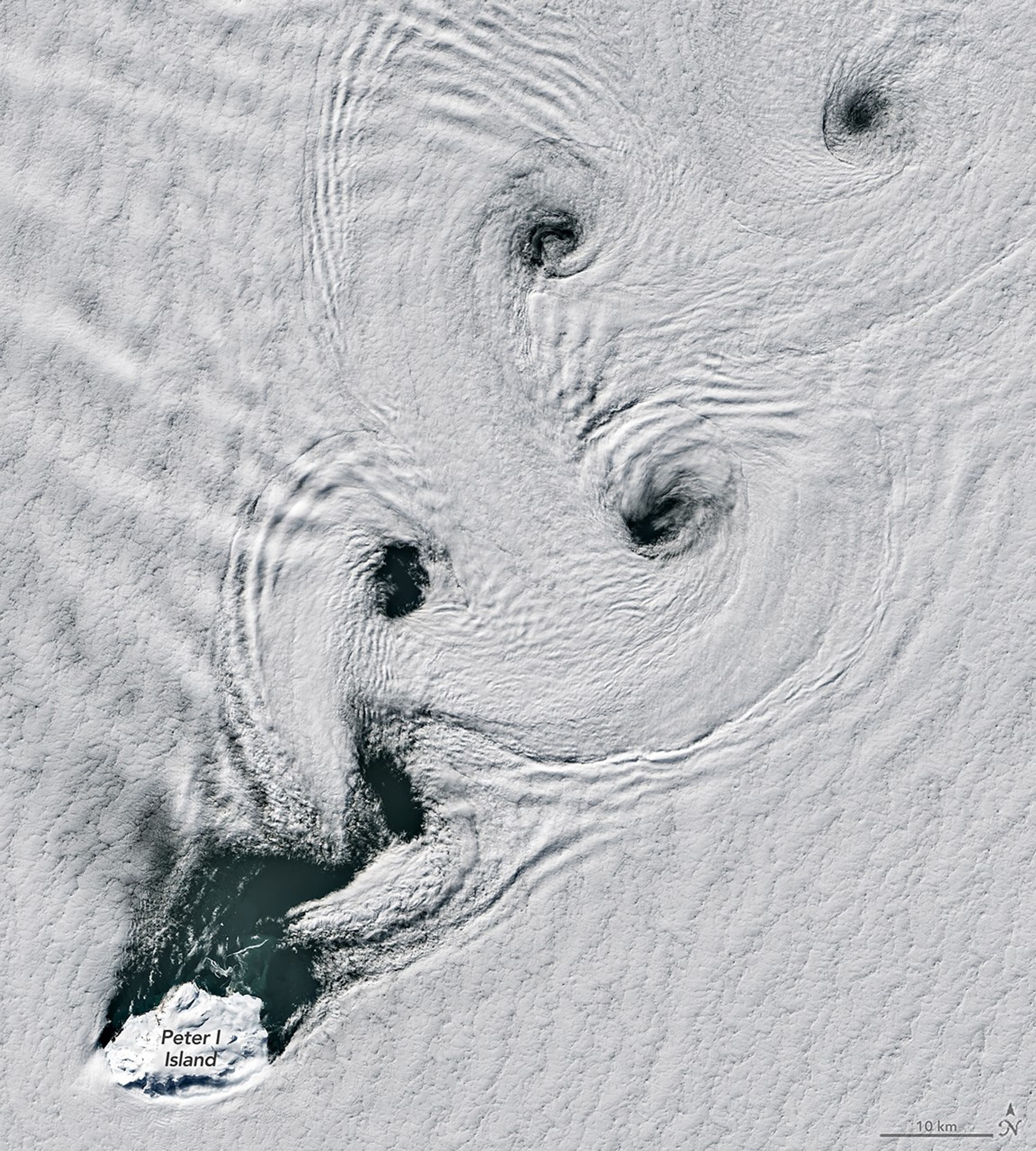 Satellite image showing von Kármán vortex streets forming spinning cloud patterns over Peter I Island in Antarctica.