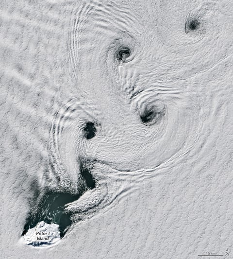 Satellite image showing von Kármán vortex streets forming spinning cloud patterns over Peter I Island in Antarctica.