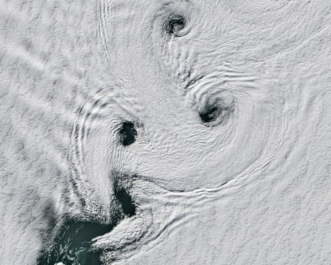 Satellite image showing von Kármán vortex streets forming spinning cloud patterns over Peter I Island in Antarctica.