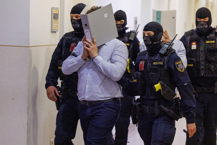 A defendant in handcuffs hides his face behind a folder while escorted to the courtroom in Wiener Neustadt, Austria, during the Taylor Swift Vienna terror plot trial