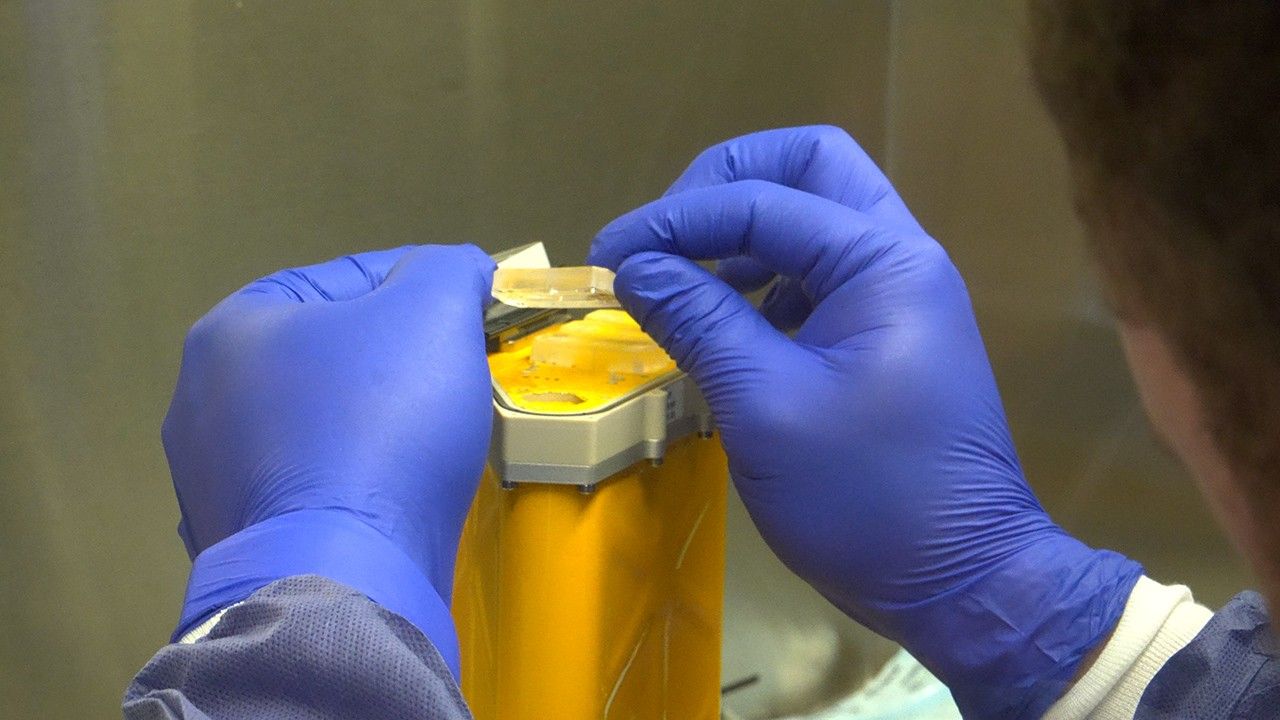 Scientist in blue gloves holds a small cylindrical AVATAR organ chip containing Artemis II astronaut bone marrow cells after their journey around the Moon