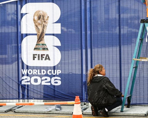 Workers affixing FIFA World Cup 2026 logos on fencing outside SoFi Stadium in Inglewood California