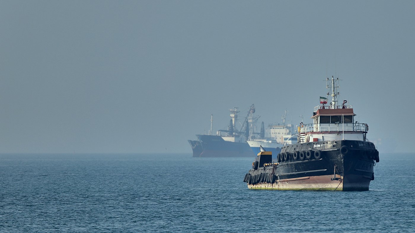 An Iranian tugboat in the Strait of Hormuz as cargo ships sit at anchor, May 4, 2026, illustrating the global shipping disruption at the center of US-Iran nuclear deal talks
