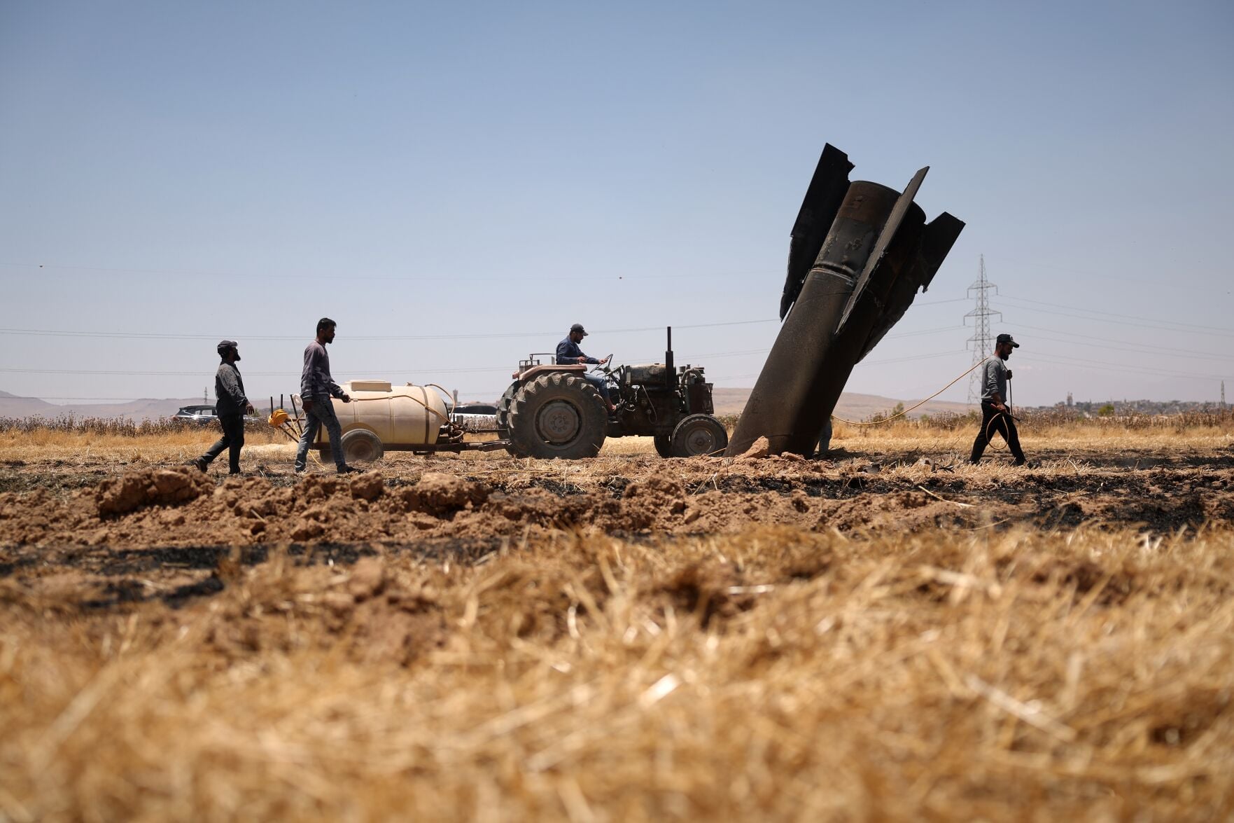 Farmers spray water in a burned agricultural field next to Iranian missile debris near the town of Najha Syria June 8 2026