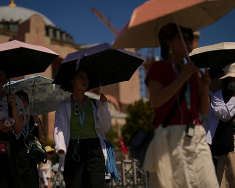 Tourists use umbrellas to shield themselves from intense sun outside Istanbul's Hagia Sophia during a summer 2025 heatwave
