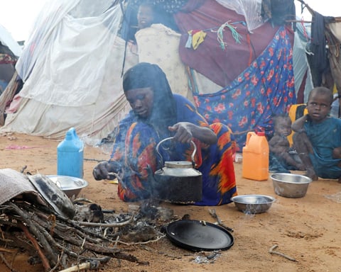 An internally displaced woman prepares breakfast outside a makeshift shelter in the Kahda district of Mogadishu, Somalia, as war-driven prices push families into hunger