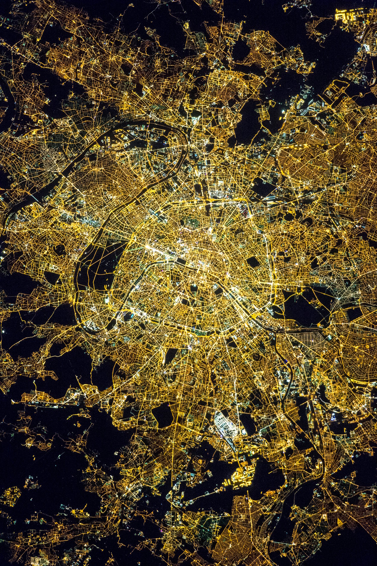 NASA astronaut photograph of Paris at night showing the Seine River as a thin black line with the bright Avenue des Champs Elysees and the radial street pattern around the Arc de Triomphe