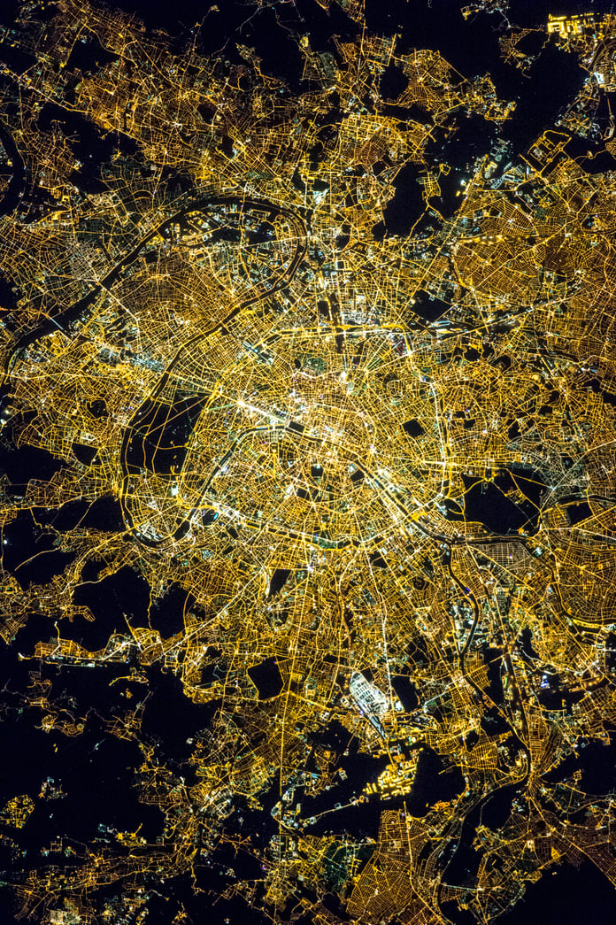 NASA astronaut photograph of Paris at night showing the Seine River as a thin black line with the bright Avenue des Champs Elysees and the radial street pattern around the Arc de Triomphe