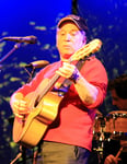 Paul Simon performing on stage with acoustic guitar at a live concert