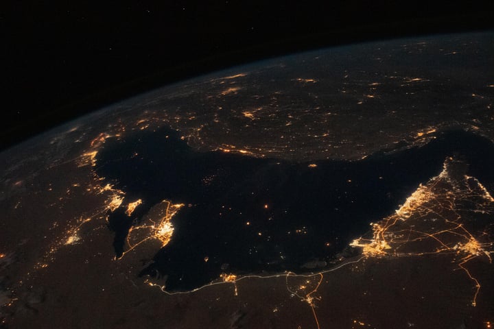 NASA astronaut photograph from the International Space Station of the Persian Gulf at night with the cities of Tehran, Dubai, Doha, Riyadh, Bahrain, and Kuwait City visible as bright clusters along the shoreline