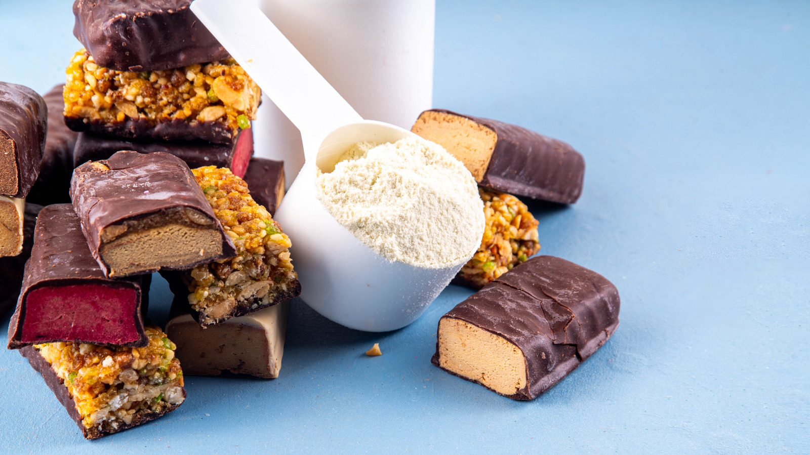 Assorted protein bars stacked next to a cup of protein powder on a gym surface