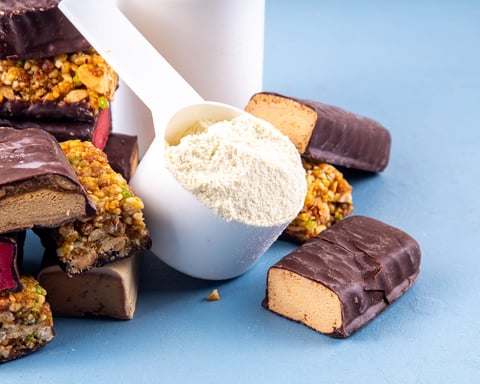 Assorted protein bars stacked next to a cup of protein powder on a gym surface
