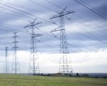 High-voltage power transmission lines against a blue sky representing the challenge of managing complex renewable energy grids