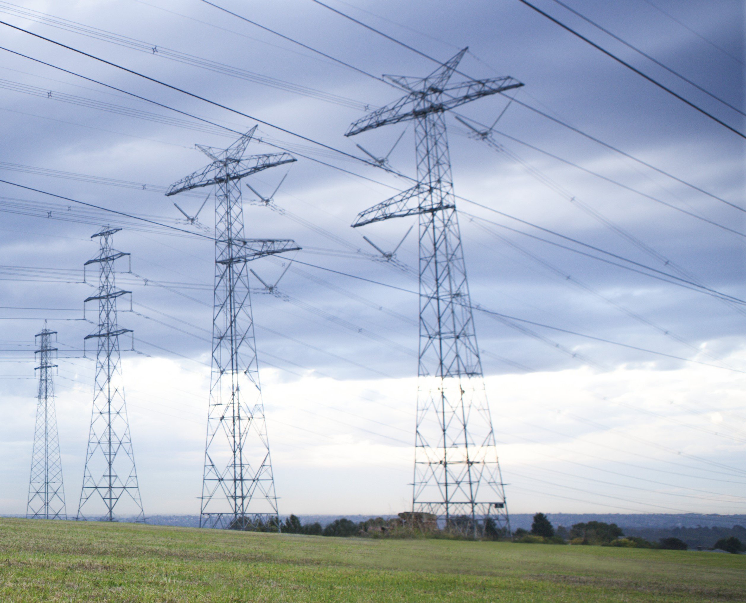 High-voltage power transmission lines against a blue sky representing the challenge of managing complex renewable energy grids