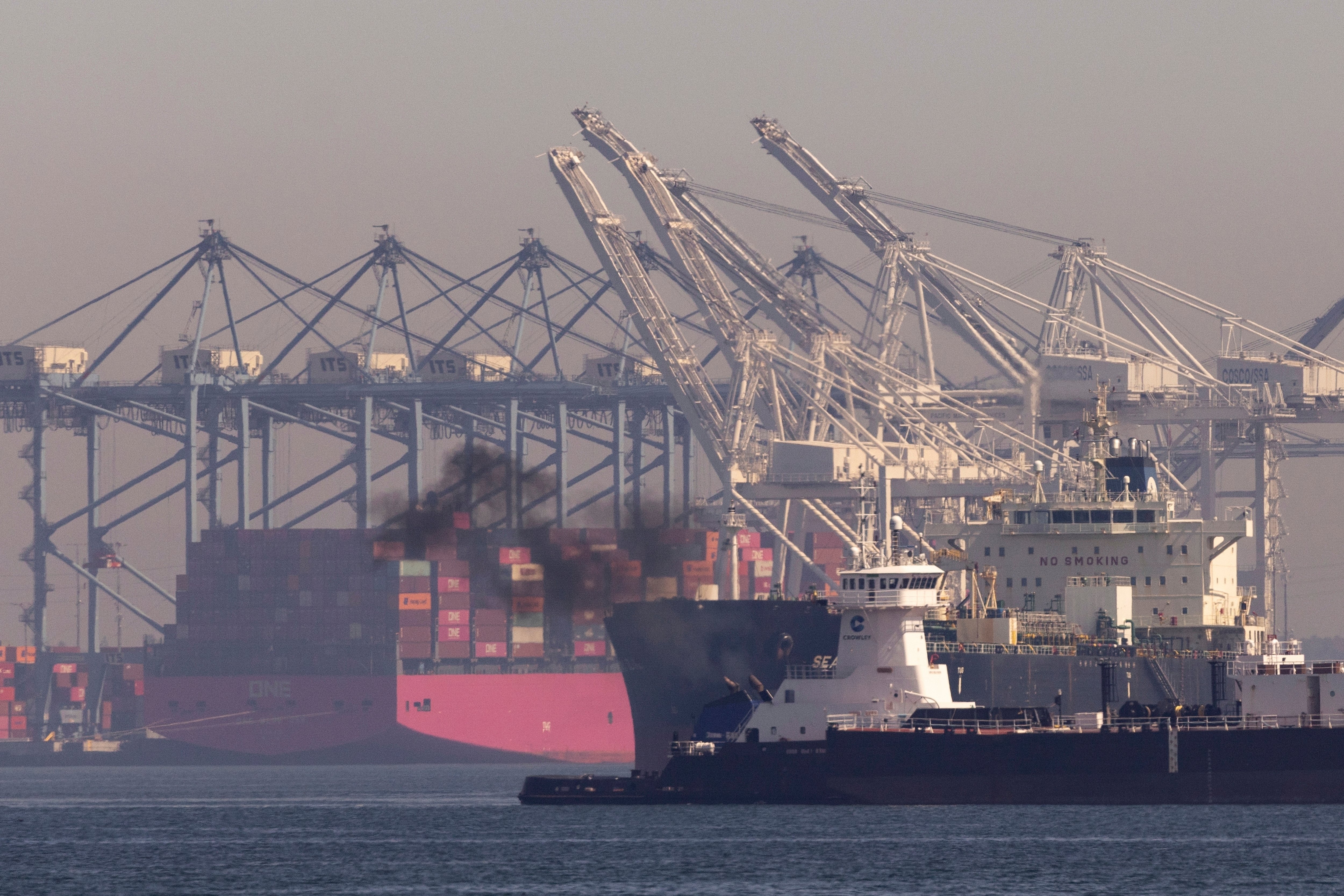 Pollution rises from a ship cruising past the Port of Long Beach in San Pedro, California, where tankers and container ships enter and exit