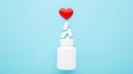 Heart medication pills spilling from bottle on blue background