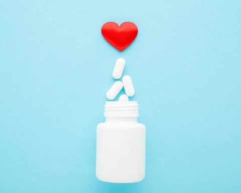 Heart medication pills spilling from bottle on blue background