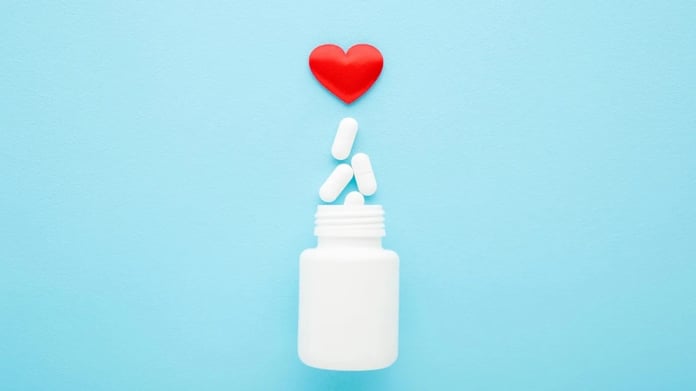 Heart medication pills spilling from bottle on blue background