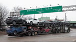 A truck transporting cars beneath signage indicating US trade routes