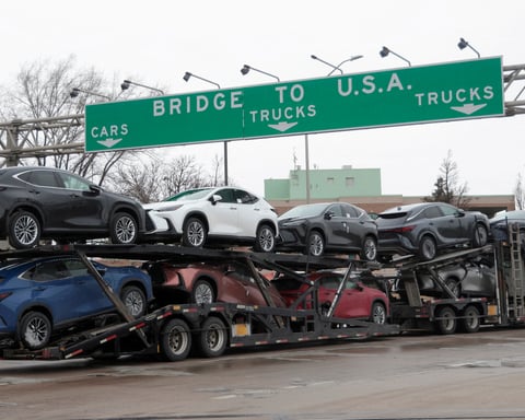 A truck transporting cars beneath signage indicating US trade routes