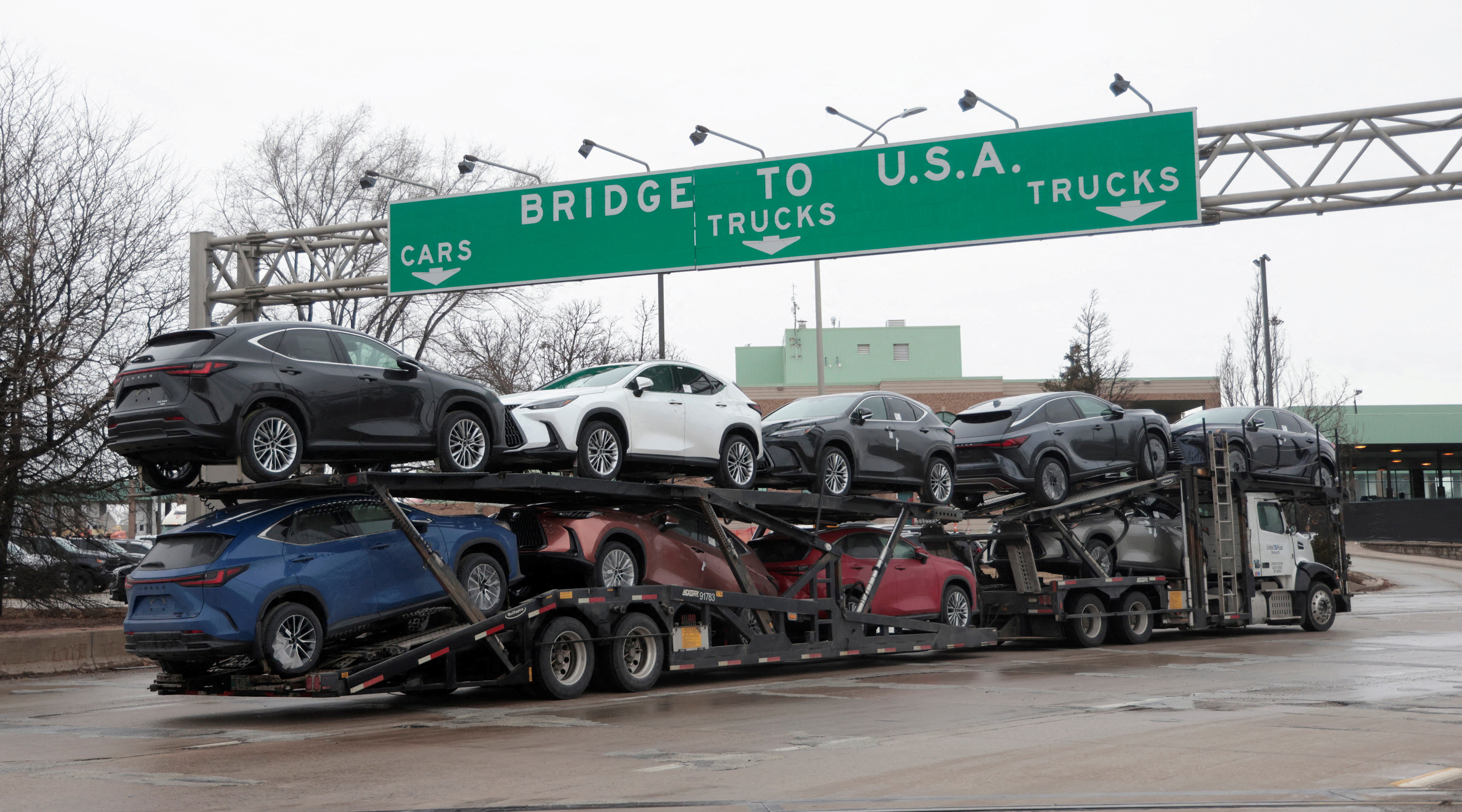A truck transporting cars beneath signage indicating US trade routes