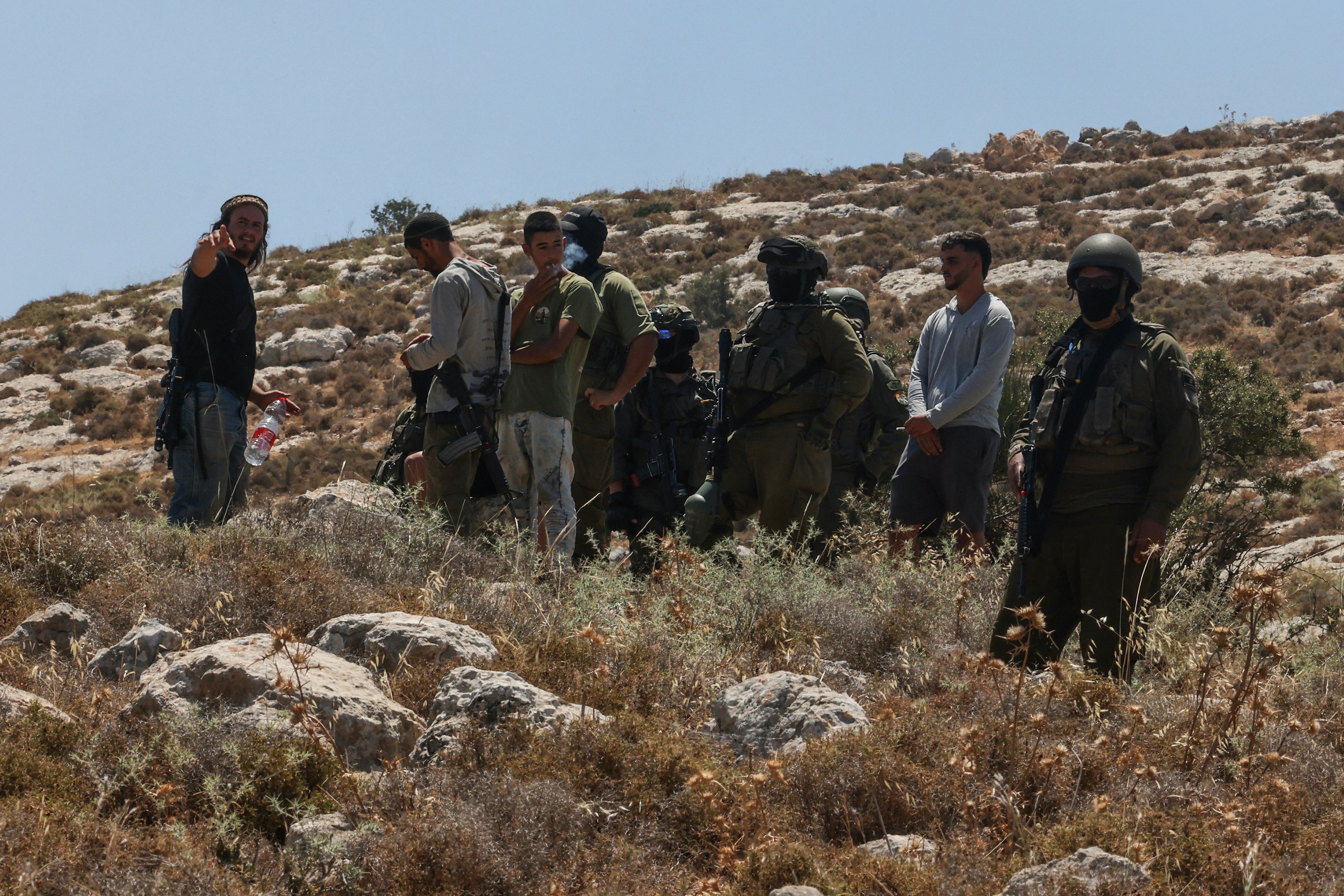 Israeli forces and armed settlers guard a bulldozer operating on Palestinian land near Dura, west of Hebron, in the occupied West Bank
