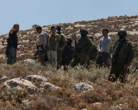Israeli forces and armed settlers guard a bulldozer operating on Palestinian land near Dura, west of Hebron, in the occupied West Bank