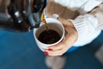 Woman's hand holding a white mug with coffee being poured in, illustrating Cedars-Sinai's largest study on coffee and liver cancer risk