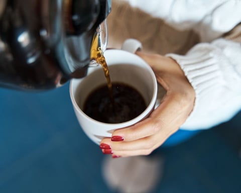 Woman's hand holding a white mug with coffee being poured in, illustrating Cedars-Sinai's largest study on coffee and liver cancer risk