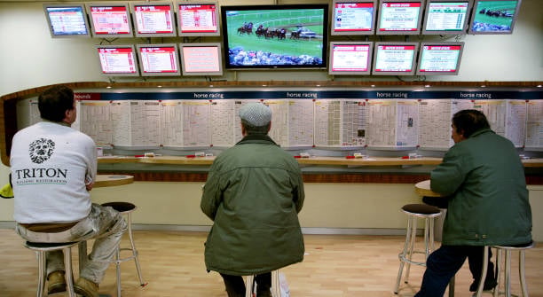 Customers seated inside a Ladbrokes Coral betting shop watching horse racing on television screens, London