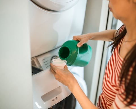 A dryer sheet resting on folded laundry beside a home clothes dryer, illustrating the everyday products oncologists say may emit undisclosed fragrance chemicals
