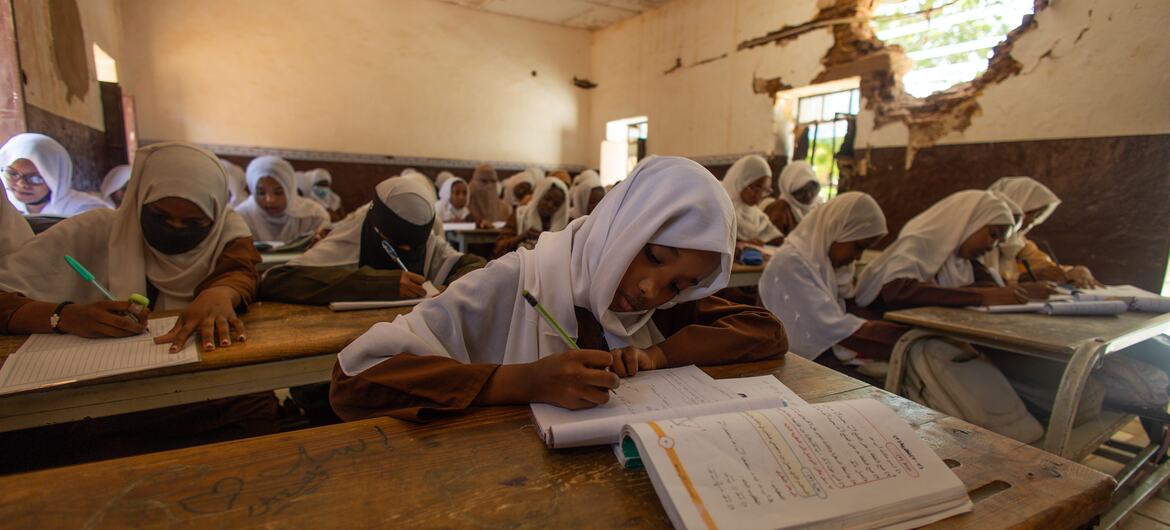 Sudanese schoolgirls writing in notebooks in a war-damaged classroom, Sudan 2026