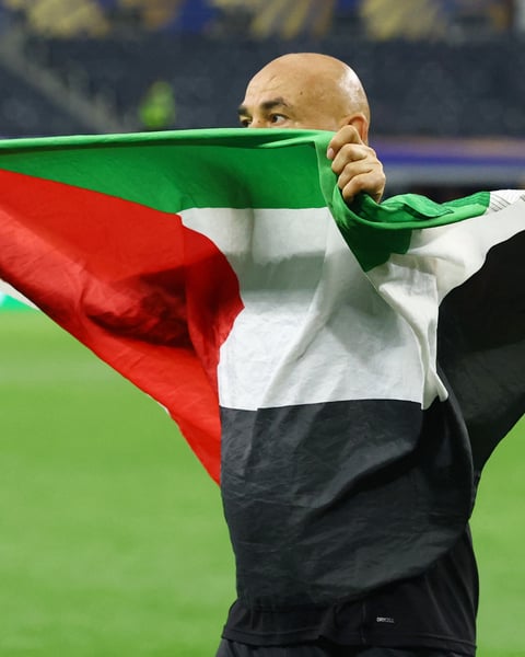 Egypt coach Hossam Hassan carries Egyptian and Palestinian flags onto the AT&T Stadium pitch after Egypt's historic World Cup knockout win over Australia